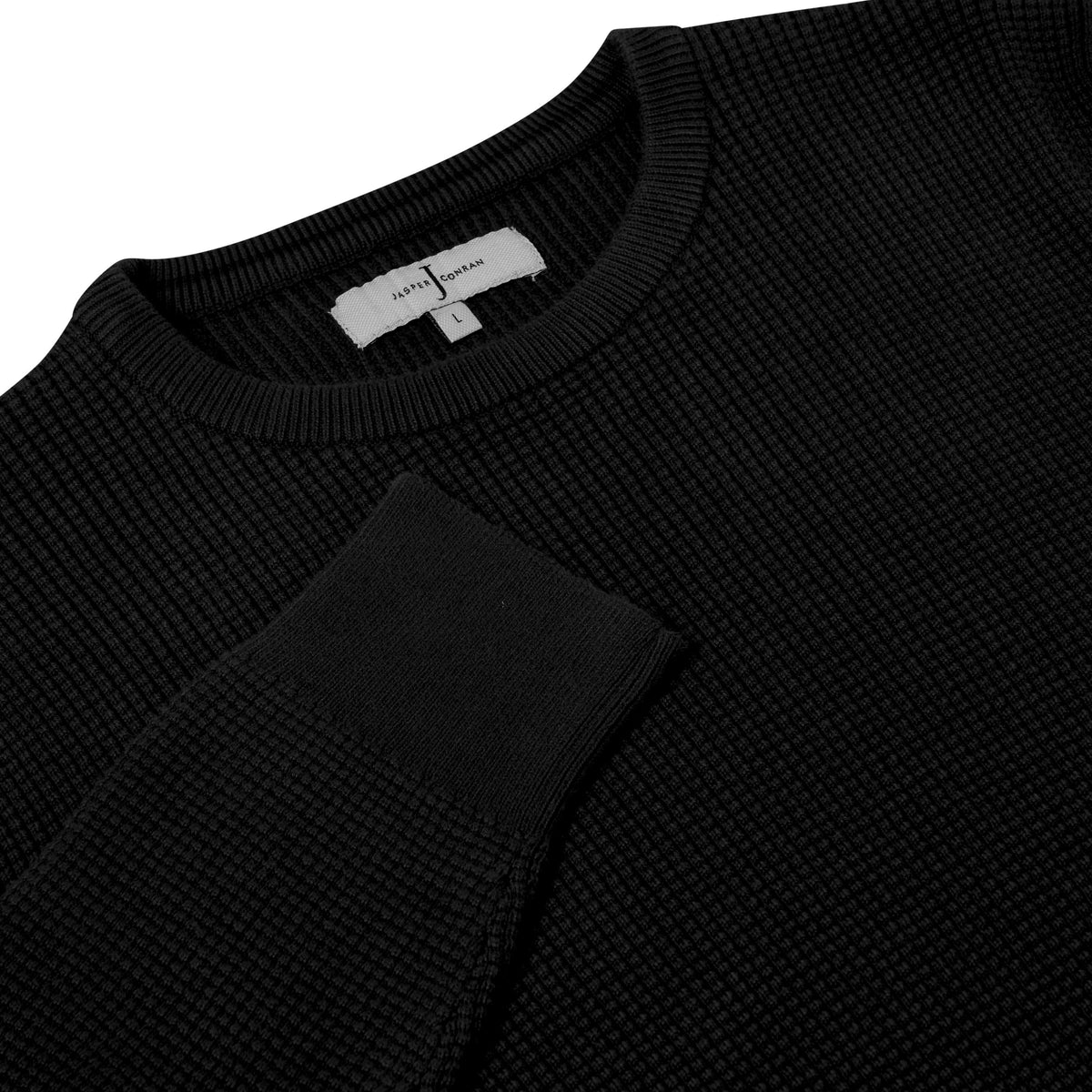 Close-up of a black ribbed knit crewneck sweater with a white neck label reading 'SWEATSHIRT' and size 'L'.
