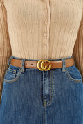 Close-up of a person wearing a beige button-up shirt and blue jeans with a brown belt featuring a gold buckle.