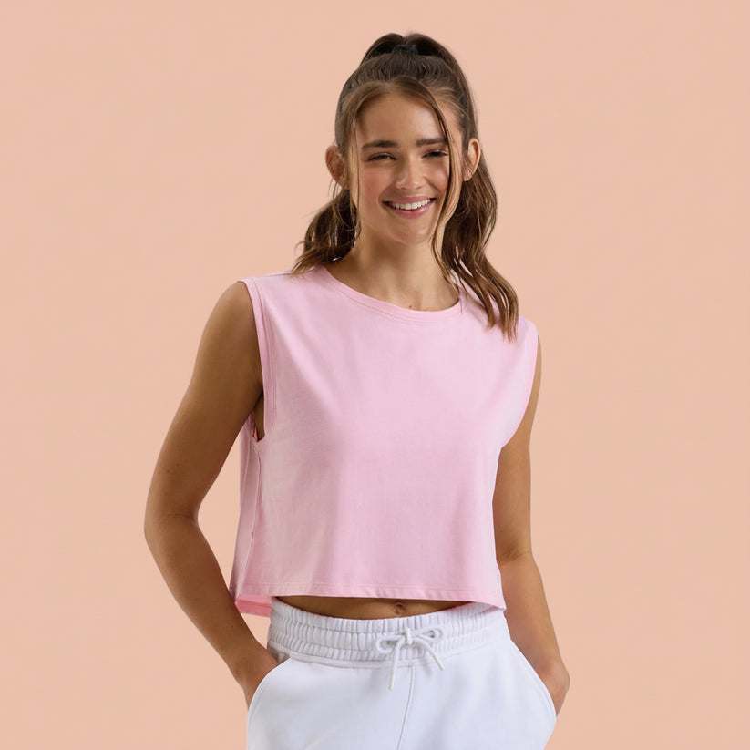 Woman wearing a pink sleeveless top and white pants on a peach background