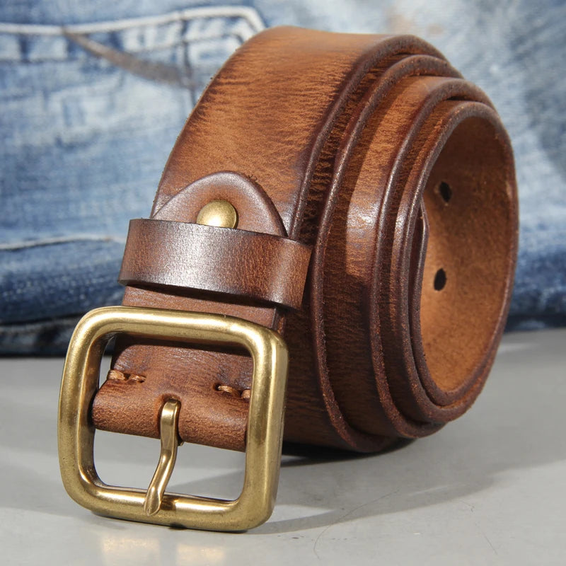 Brown leather belt with gold buckle on a gray surface with jeans in the background