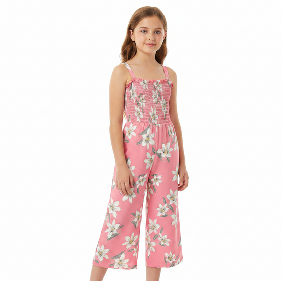 A young girl modeling a pink floral jumpsuit with a smocked bodice and wide legs, set against a plain white background.