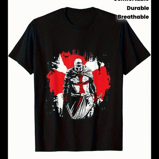 A black short-sleeve t-shirt with a graphic print of a knight in armor holding a sword, set against a red and white splattered background. The text 'Deus Vult' is printed in a white gothic font above the graphic.