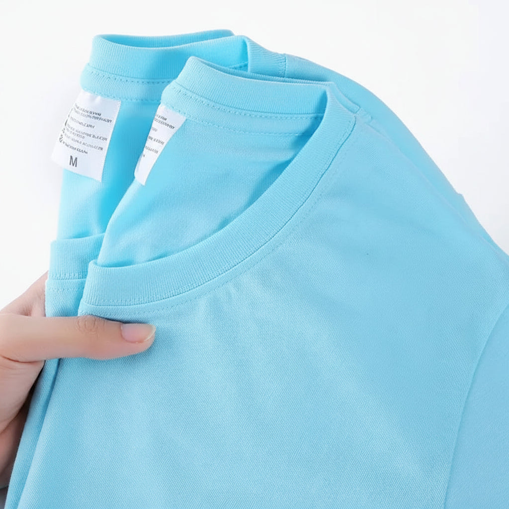 Light blue t-shirt held by a hand with visible label on a white background