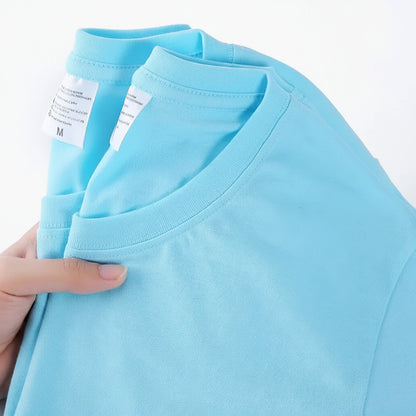 Light blue t-shirt held by a hand with visible label on a white background