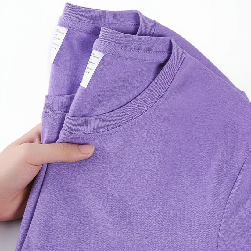Purple t-shirt with a hand holding it, showing a label on a white background.