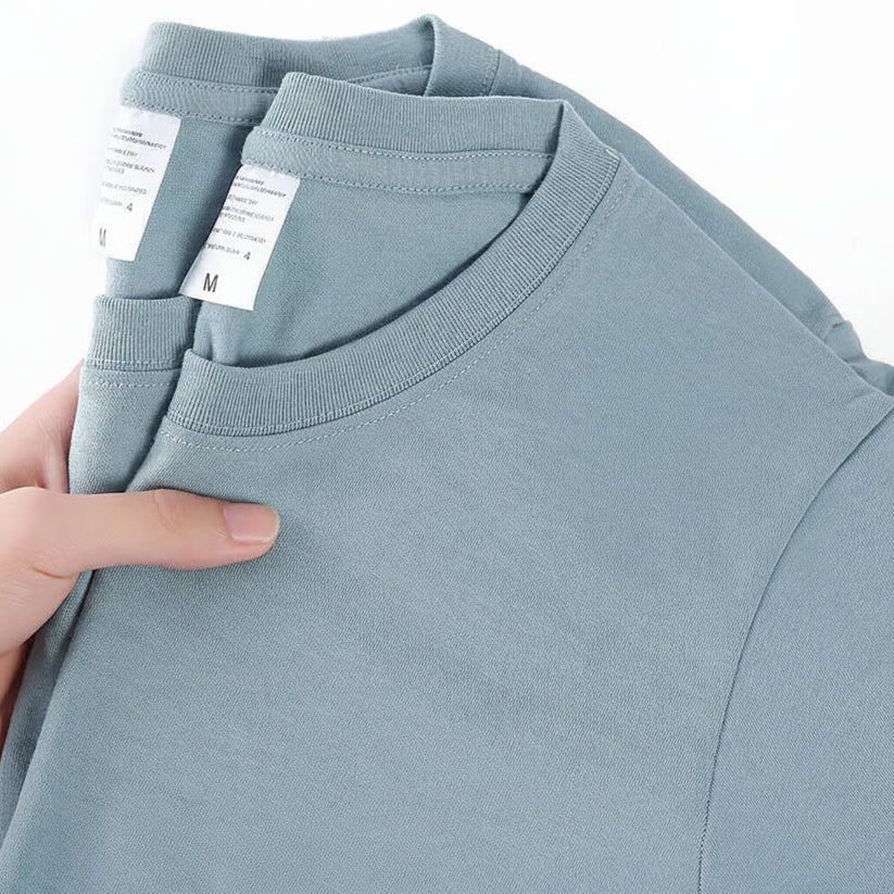 Light blue t-shirt with a hand holding it, showing a close-up of the fabric and tag.