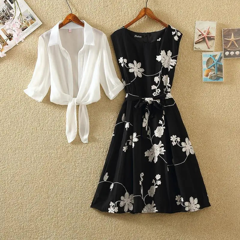 Black dress with floral embroidery and white blouse on hangers against a beige wall.