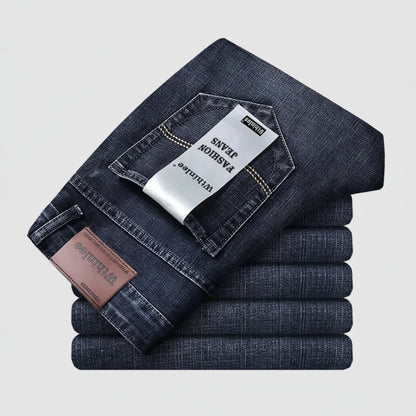 Stack of folded dark blue jeans with a visible brand tag on a light gray background