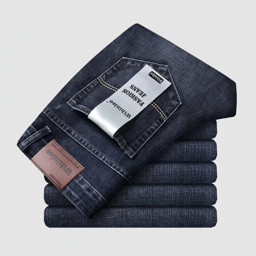 Stack of folded dark blue jeans with a visible brand tag on a light gray background