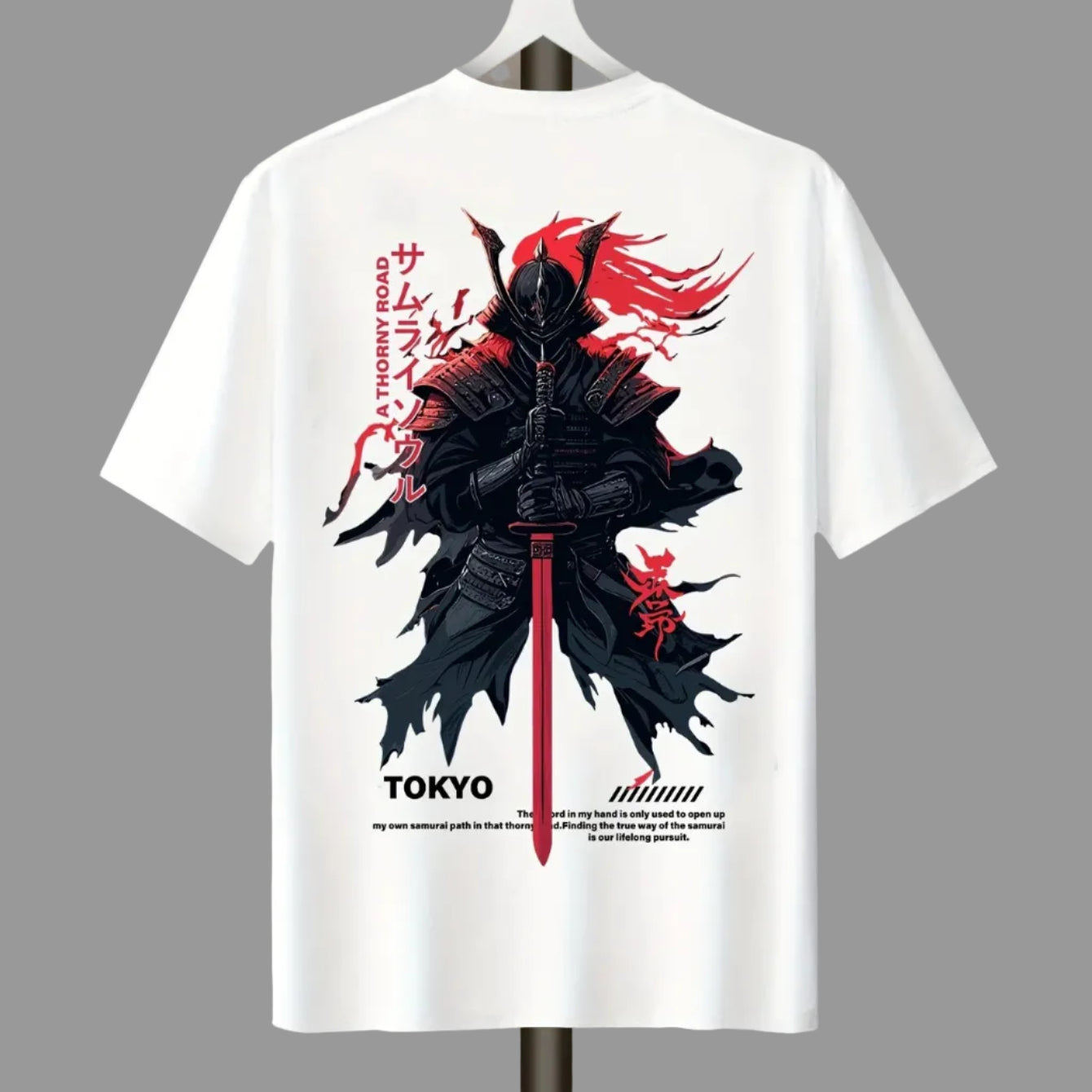 White short-sleeve T-shirt hanging on a hanger against a plain light gray wall, featuring a large back graphic of a black samurai warrior with red hair and sword, plus red Japanese text and small black text near the hem.