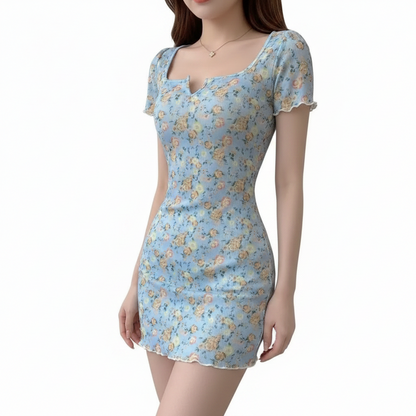 A woman wearing a light blue short-sleeve mini dress with a delicate floral print, featuring a square neckline with a small keyhole cutout and ruffled trim.