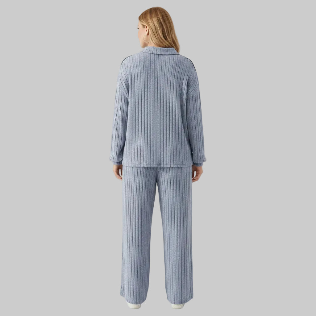 Person wearing a blue ribbed pajama set in a room with white walls and wooden floor.