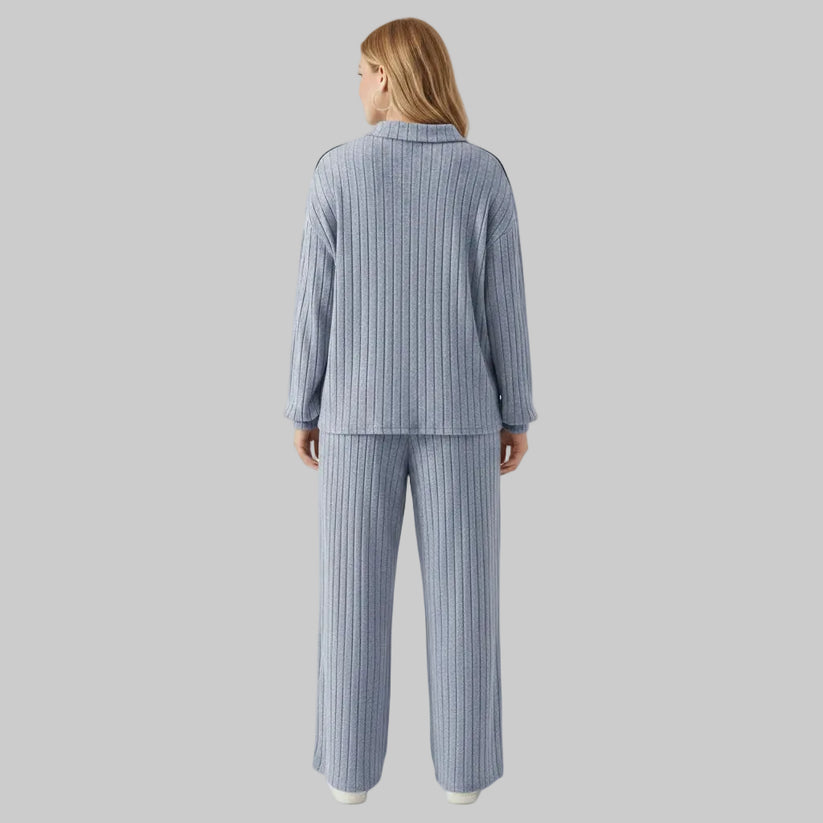 Person wearing a blue ribbed pajama set in a room with white walls and wooden floor.