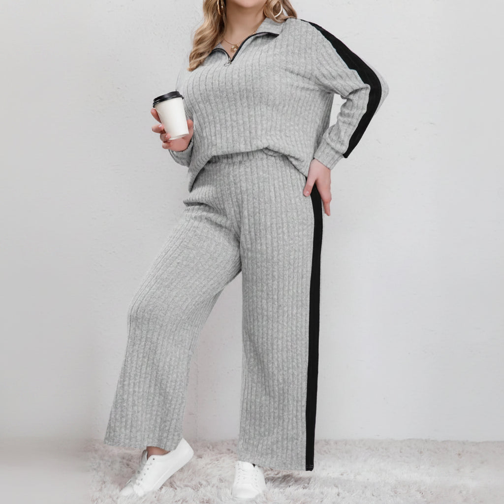 Woman wearing a gray knit outfit with black side panels, holding a coffee cup.
