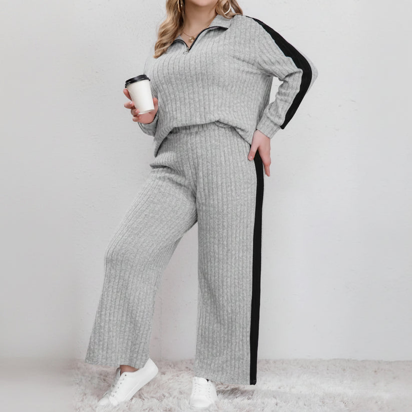 Woman wearing a gray knit outfit with black side panels, holding a coffee cup.