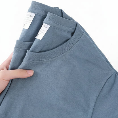 Blue t-shirt held by a hand with visible label, on a white background