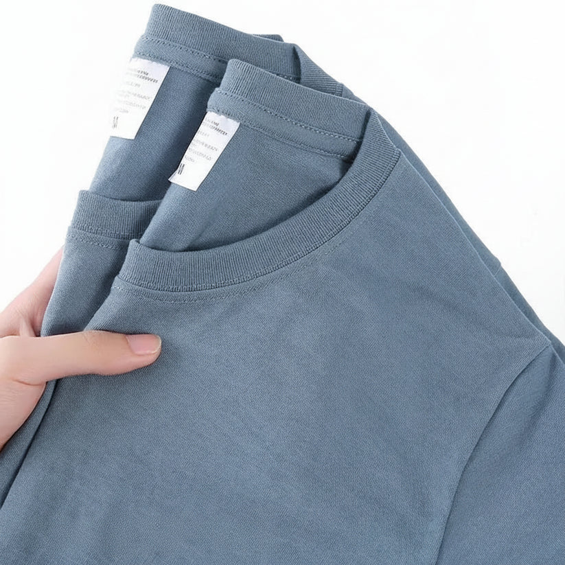 Blue t-shirt held by a hand with visible label, on a white background