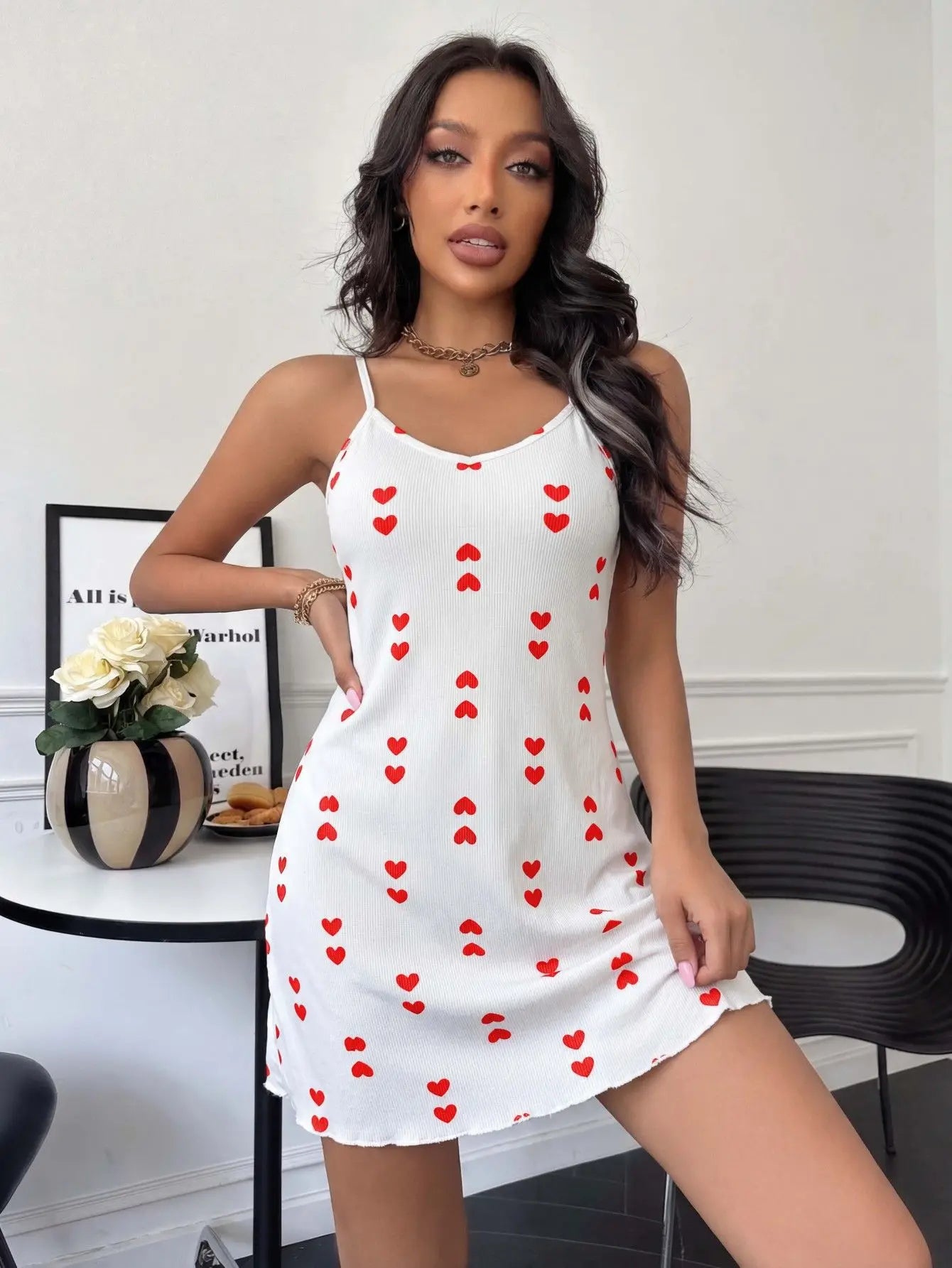 Woman wearing a white dress with red heart patterns in a room.