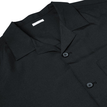 Close-up of a black short-sleeve button-up shirt with a pointed collar and dark buttons, laid flat against a white background.