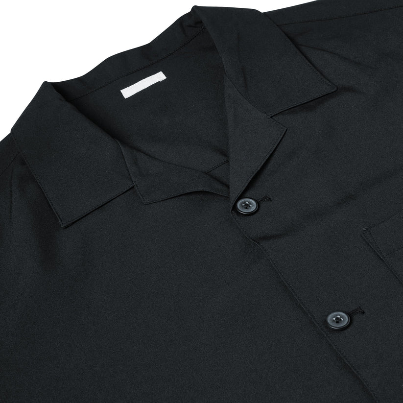 Close-up of a black short-sleeve button-up shirt with a pointed collar and dark buttons, laid flat against a white background.