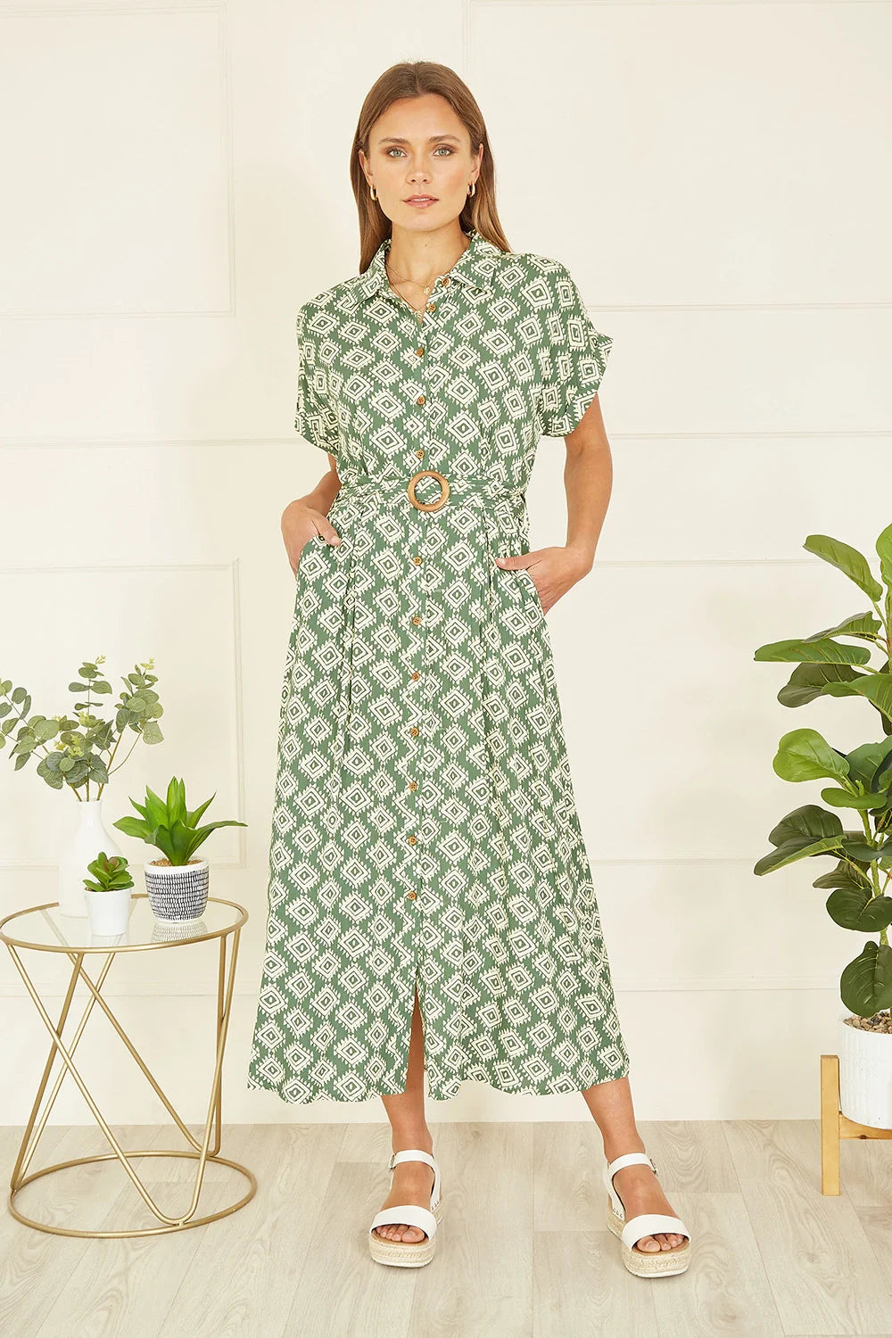 Woman wearing a green patterned dress in a room with plants